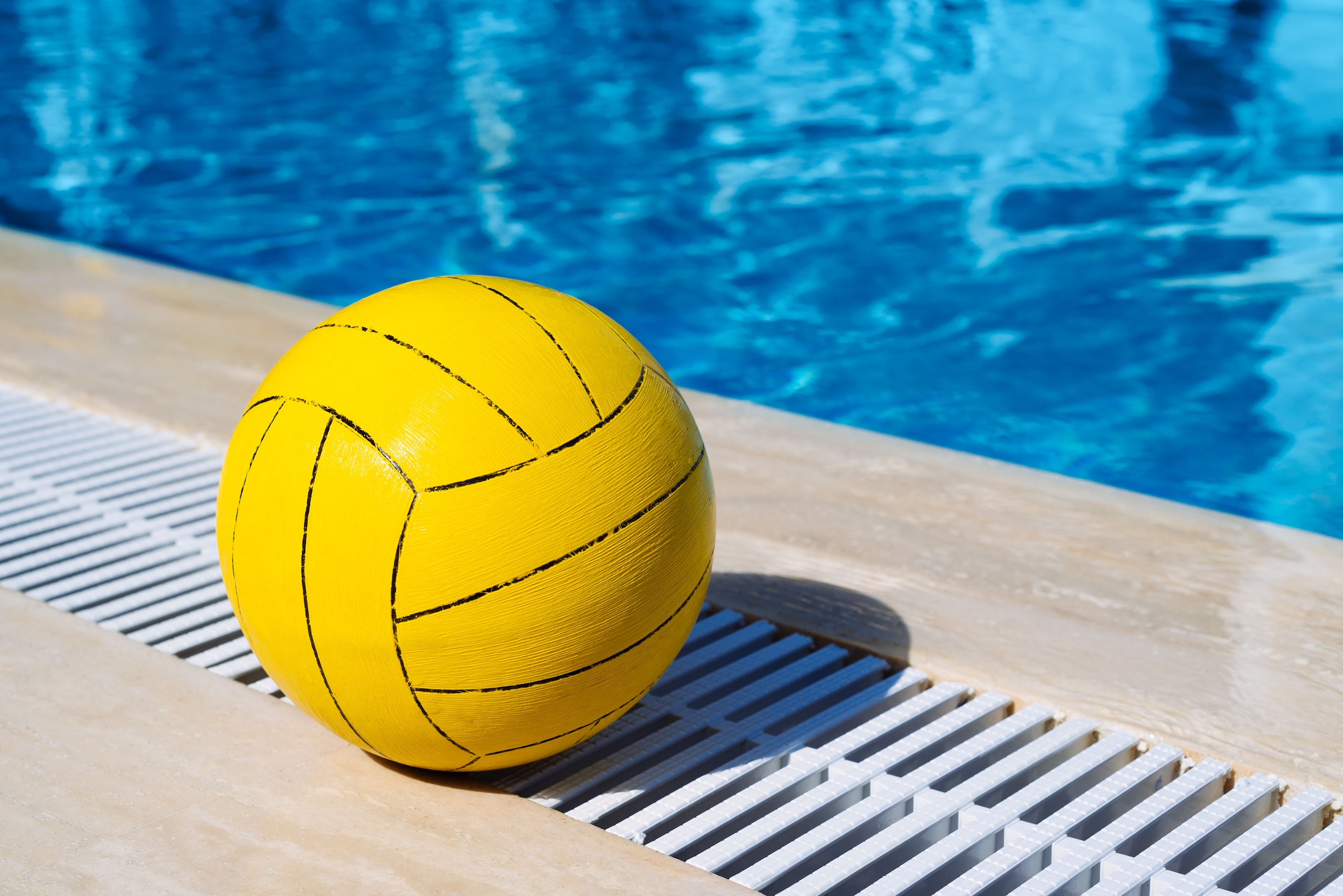 Summer games in the pool. Yellow ball on a background of blue water in a sunny resort